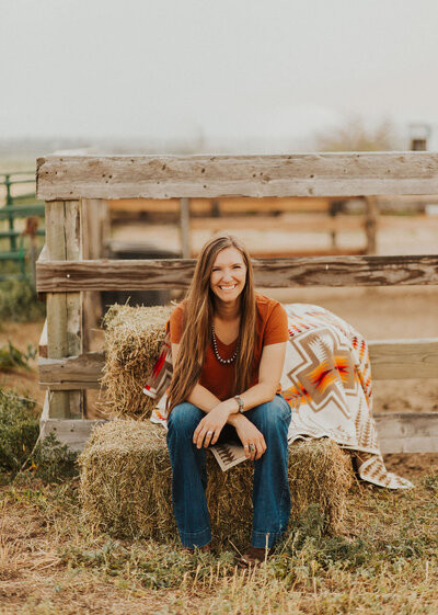 woman with long dark hair sitting on a hay bale