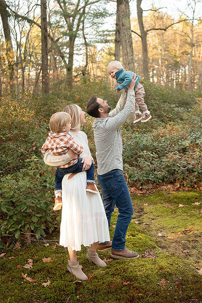A dad is throwing his son in the air while his mom watches at a photo session in Whip Hill Park in Stoneham.