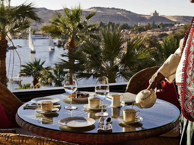 Tea being served at an outdoor table overlooking the Nile River with palm trees and sailboats in the background.
