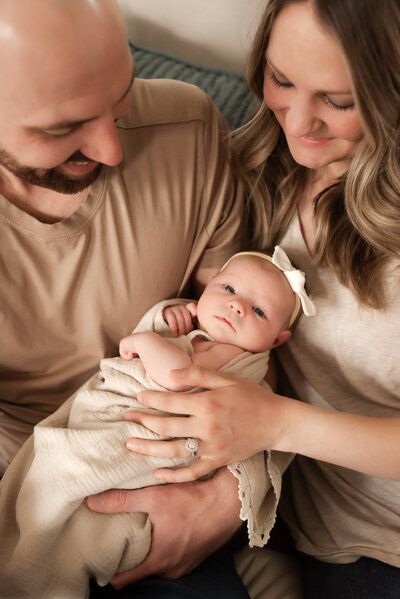 A mother and father hold and smile at their newborn baby.