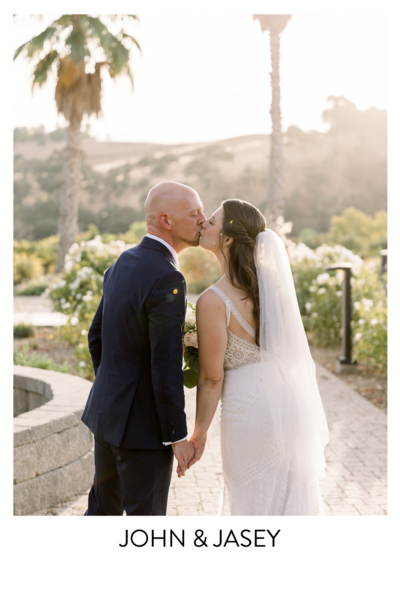 White Barn Wedding Couple stands smiling at each other on their wedding day holding beautiful peach and cream colored flowers
