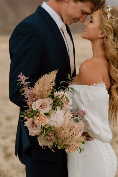 bride hugging the back of her grooms neck surrounded by red rock formations in Utah at golden hour