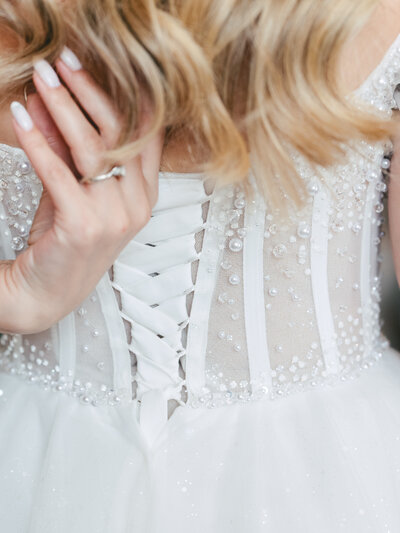 Close up of a delicate white lace corset wedding dress back with pearl beading and blonde wavy hair.