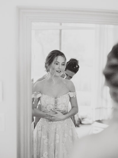 Black and white photo of bride's mother zipping up her dress