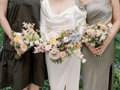 A close up of a bride's arms holding her bouquet in dusty pink and peach blooms and with a little bit of blue flowers.