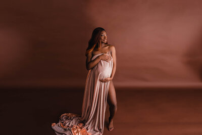 pregnant black woman in silk gown holding her belly in photoshoot in Cleveland Ohio