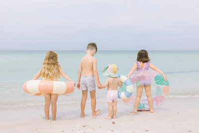 Four kids on the beach facing the ocean and holding inner tubes