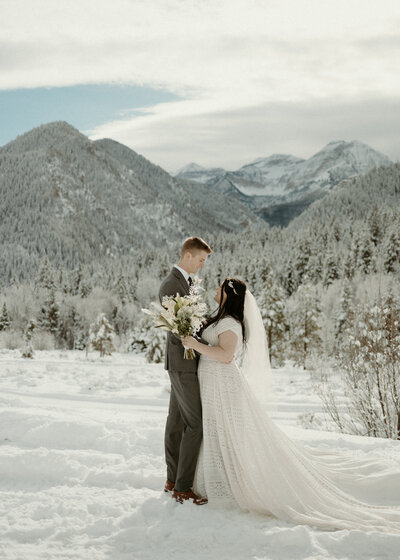 Bride and groom with their arms wrapped around each other's waists in the snowy mountains of Orem, Utah.