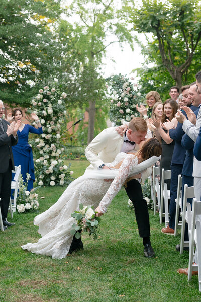 Bride and groom share a romantic dip kiss in the aisle at their wedding ceremony, surrounded by joyful guests. The elegant event was planned and designed by Blue Sapphire Events, a Washington, D.C.–based wedding planner.