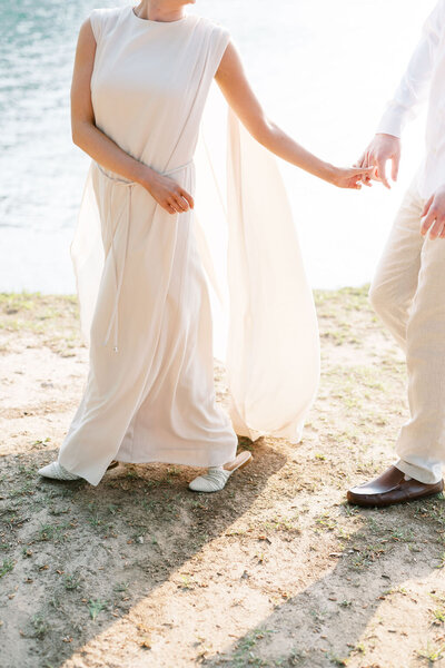 Bride and groom walk hand in hand together on the shores of Lake Lanier