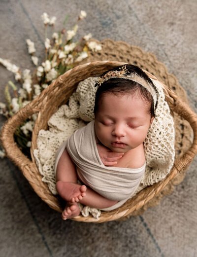 Artistic newborn photography by Stamford CT photographer capturing baby girl with floral headband in woven basket with delicate styling
