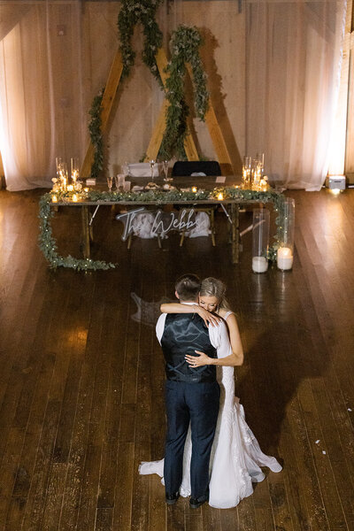 Bride and groom sharing their first dance on a wooden floor in front of a candlelit sweetheart table with greenery at Bear Ridge Destination.