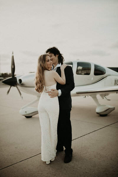 engaged couple holding each other at a airport with plane behind them in Jacksonville, FL