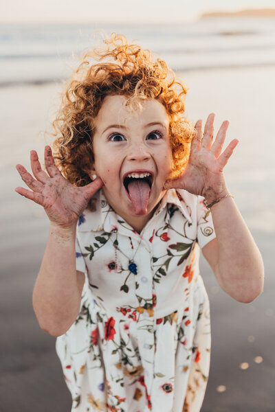 a cute red headed girl makes a silly face at the camera during her family photos taken on a beach in San Diego