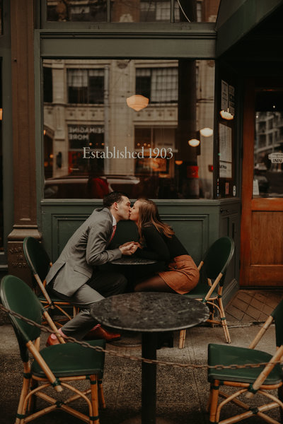 Man and woman kiss across a table in downtown Seattle during their engagement session