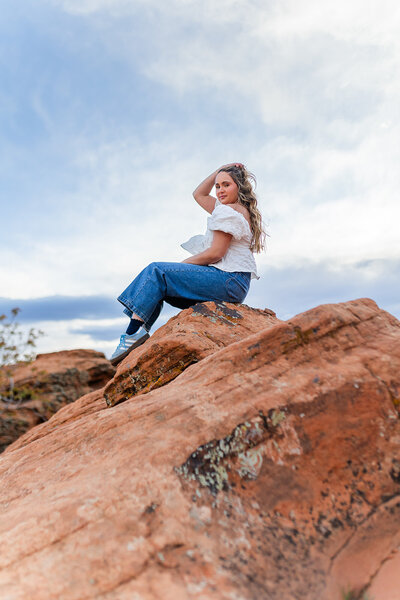 girl sitting on red rocks and holding her hair back for photos in st george