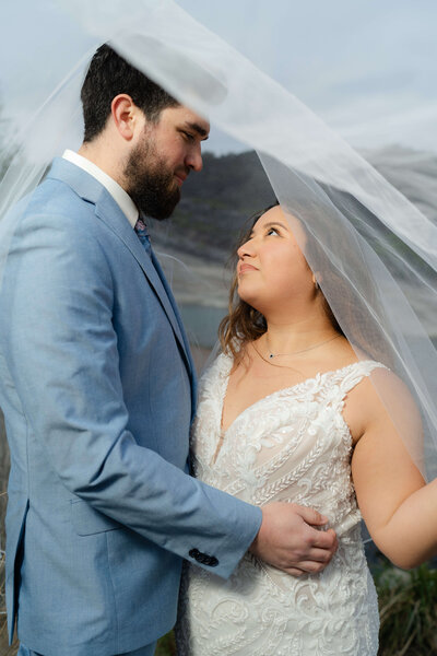 couple laughing and smiling at each other during their adventure session on a mountain top