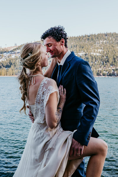 Bride and groom sharing a kiss in an open field under a double rainbow, with dramatic storm clouds in the background during their elopement