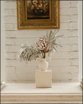 Dried flowers in an ornate vase in front of a white brick wall in a studio rental space.