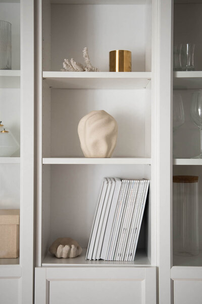 A white bookcase filled with colorful books and decorative vases, showcasing a blend of literature and art.