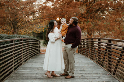 Family enjoying a cozy fall moment on a wooden bridge during a Charlotte family photography session.