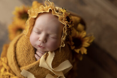 Baby wrapped, sunflowers around her