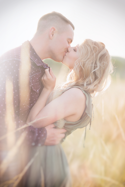 Couple kissing in a sun drenched field in the spring.