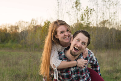 Couple laughs during piggyback ride through a meadow