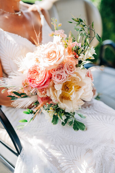 woman in white dress sitting down holding a bouquet of pink and white flowers with greenery