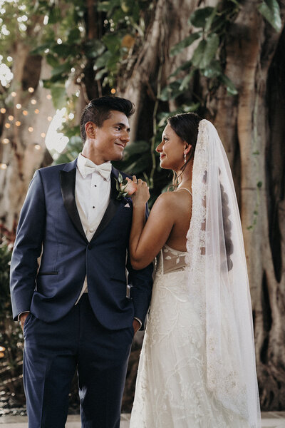 outdoor couple smiling under tree with long draping wedding veil