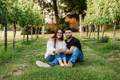 Couple casually sitting in the grass next to grape vines in a vineyard