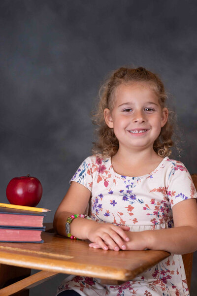 A young girl sitting at a desk with hands folded. 