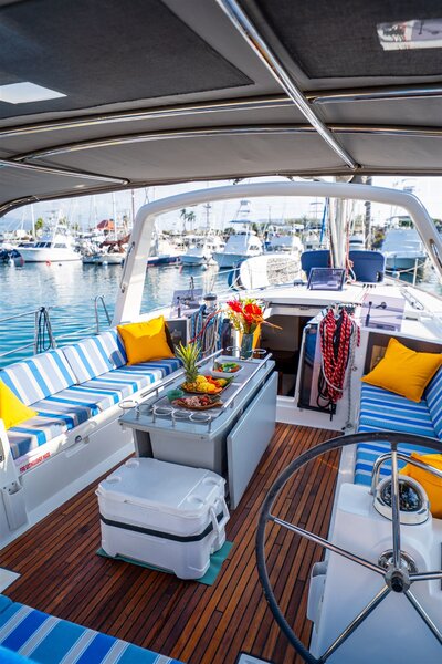 Beautifully styled sailboat interior in Hawaii with blue striped seating, yellow pillows, tropical flowers, and a food platter arranged on the table while docked in the harbor.