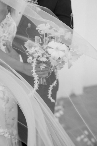 Close-up of a bride holding her bouquet, with delicate flowers and a flowing veil captured in a black-and-white portrait at Junipero Serra Museum in San Diego. This intimate moment beautifully showcases the bride’s connection to her wedding day. Felisha, a New England-based destination wedding photographer, captures timeless wedding moments in San Diego, New England, and worldwide locations.