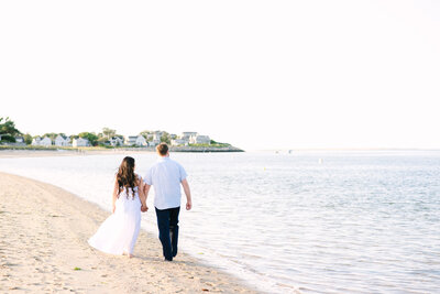 couple walking away from the camera by the ocean during their chatham lighthouse beach sunset engagement session