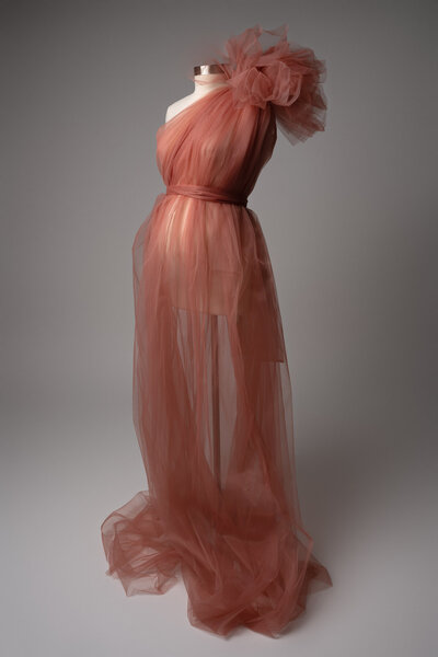 One-shoulder terracotta tulle maternity dress with large shoulder detail and sheer flowing layers