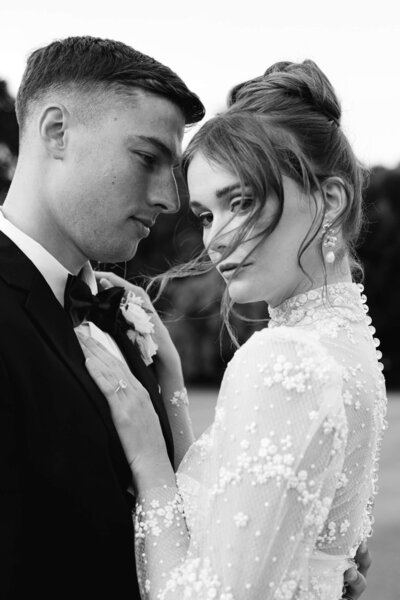 candid black and white image of a bride with her hands on the grooms chest as she looks over to the camera