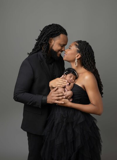 Baby sleeping on Mom's chest and Mom and Dad smiling at each other, enjoying this moment. Photographed by Jenni Nikki Photography at Marietta Newborn Photo Studio.