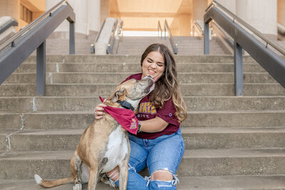 Texas State graduate sitting with dog on library steps during senior session on campus in San Marcos, Texas.