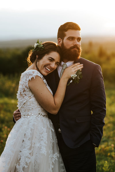 A bride lays on her groom's chest at sunset