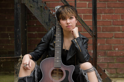 Musician influencer sitting with a guitar against a brick wall