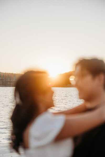 Artistic blurred photo of an engaged couple smiling at each other during their sunset engagement photoshoot at Canberra's Lake Burley Griffin. Photography by Acacia & Grace