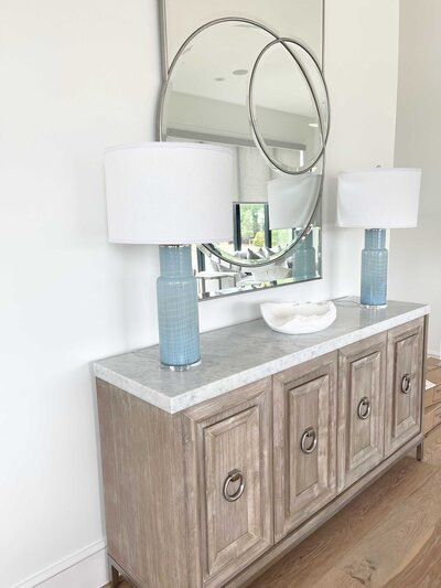 A space decorated by the best interior designers in Frisco, featuring two large aqua marine lamps and circular mirrors, showcasing the designer's professionalism and use of elegant accessories.