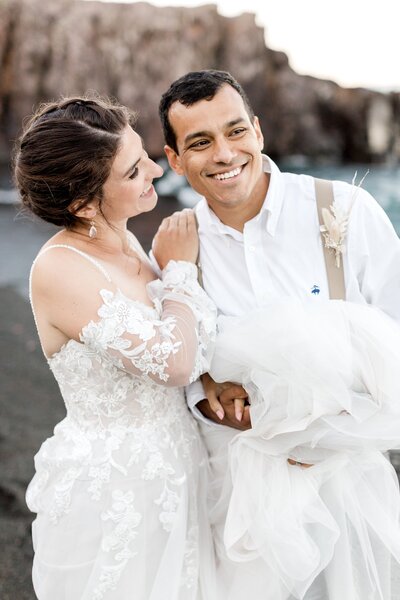 Bride and groom smile after ceremony on black sand beach Hawaii destination wedding.