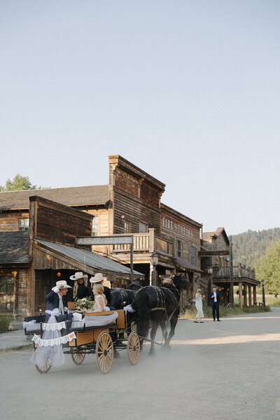 bride and groom riding on a horse drawn carriage through a western town in Big Sky