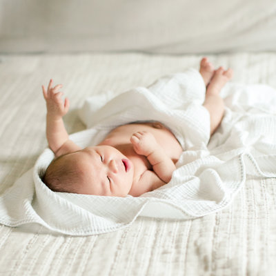 baby laying on white bedding for newborn lifestyle in home photography