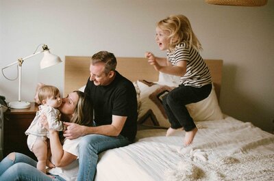 A family in Port Perry, Ontario snuggling their baby in their bedroom. The other child is jumping on the bed. 