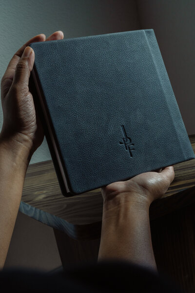 Hand holding a leather-bound photo album from JPF Galleries, capturing memories meant to last.