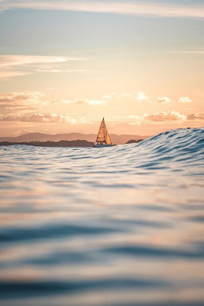 Segelboot mit gehissten Segeln in der Ferne vor der Küste bei Sonnenuntergang