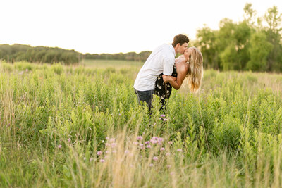 A white couple standing in a grassy field, leaning into a kiss.